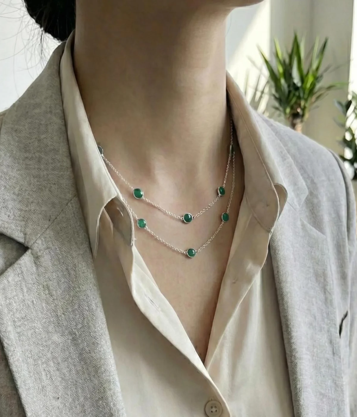 A long 925 sterling silver station necklace featuring vibrant green round gemstones set in polished silver bezel frames, elegantly displayed on a neutral fabric background within a wooden jewelry tray.