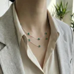 A long 925 sterling silver station necklace featuring vibrant green round gemstones set in polished silver bezel frames, elegantly displayed on a neutral fabric background within a wooden jewelry tray.